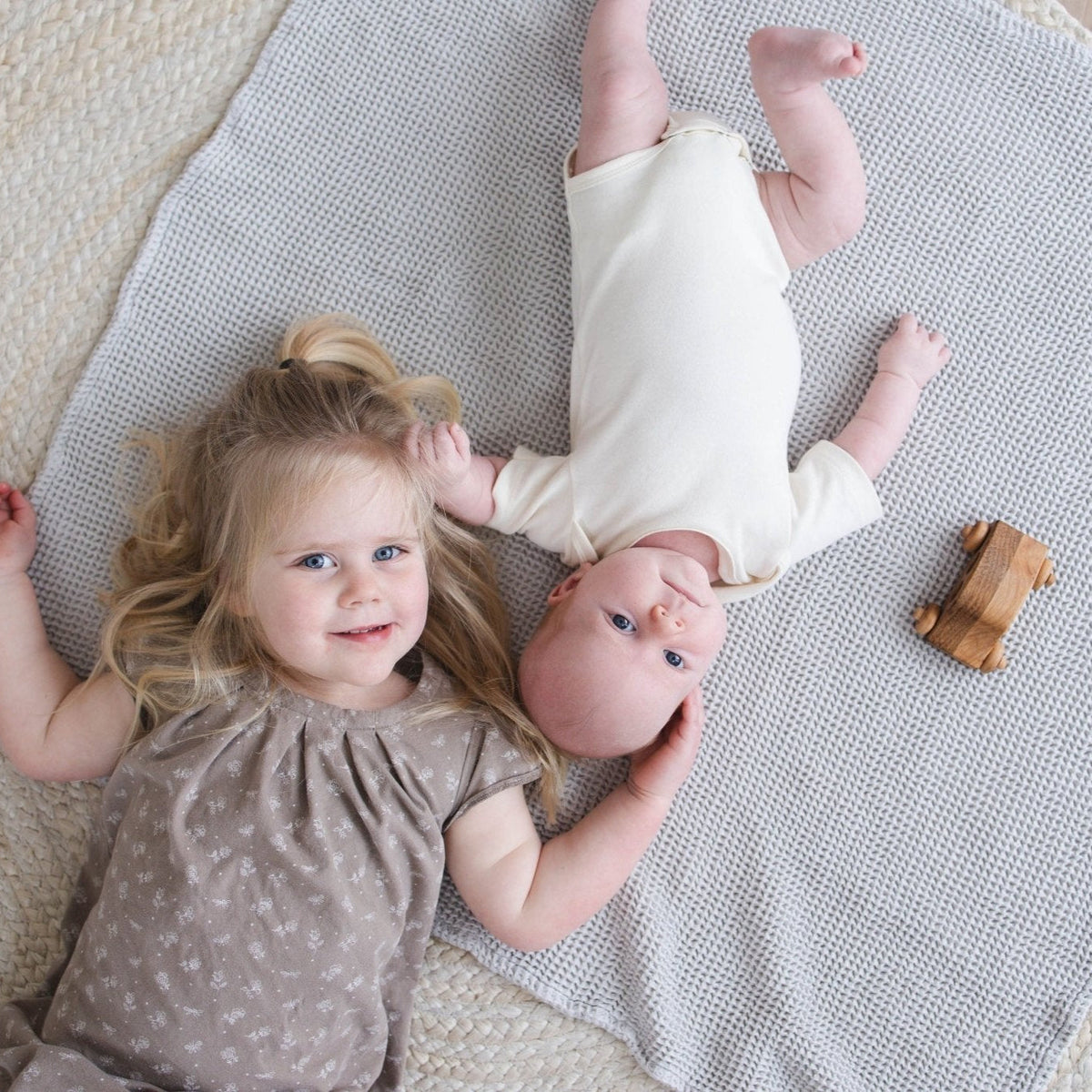 SpiritnSprout: Two children lying on a grey waffle blanket